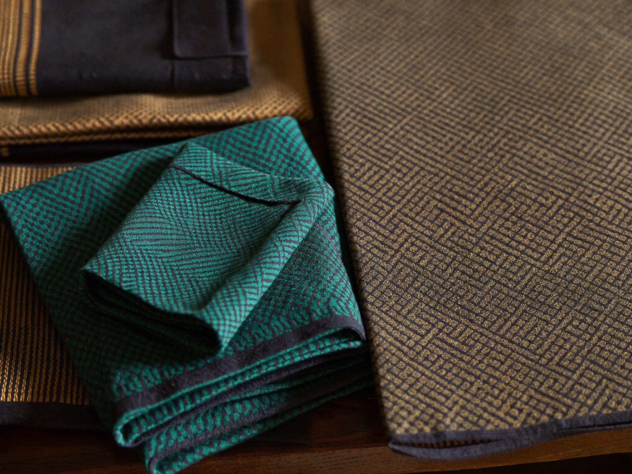 Folded kitenge fabrics in teal, navy and gold patterns stacked on a wooden table